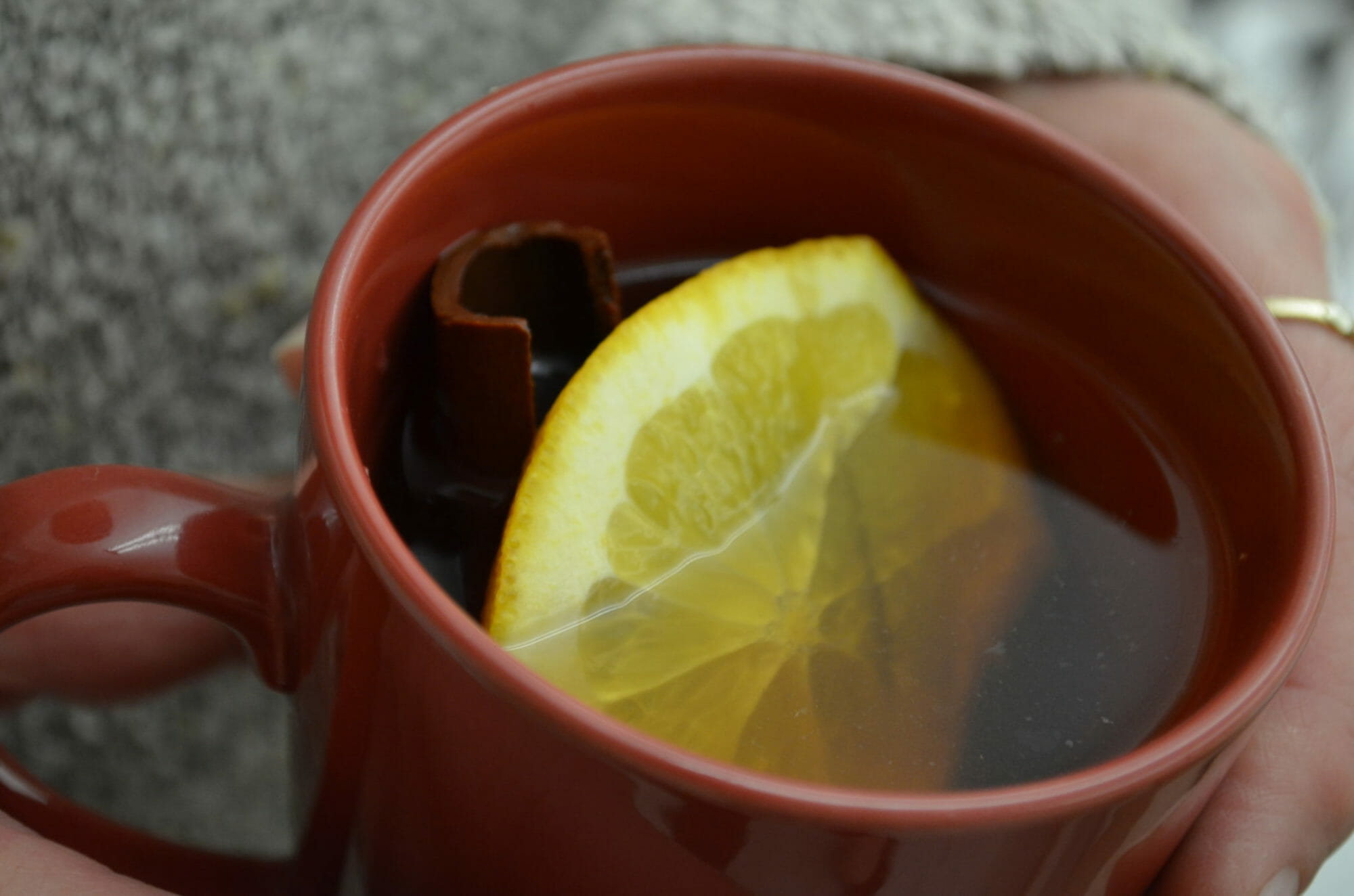 Close-up of a rust-colored mug filled with Mulled Apple Cider, a lemon wedge, and a cinnamon stick.