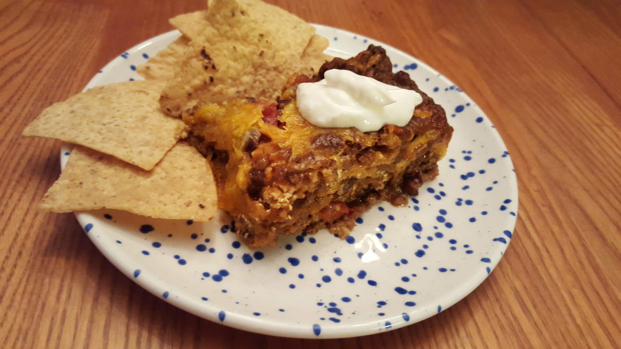 A white and blue splatter plate filled with corn chips and enchilada casserole topped with sour cream.