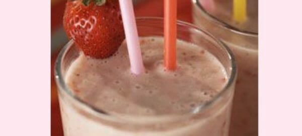 Close-up of a glass filled with a strawberry shake, two straws, and a fresh strawberry garnish.