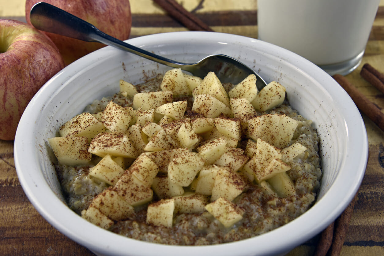 A white bowl filled with a serving of Apple Cinnamon Steel Cut Oats, topped with apple pieces and cinnamon.