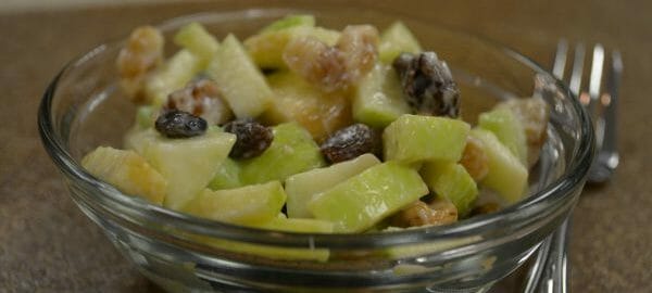 A serving of Apple Salad with raisins and walnuts in a clear bowl, with a fork nearby.