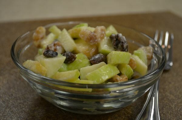 A serving of Apple Salad with raisins and walnuts in a clear bowl, with a fork nearby.