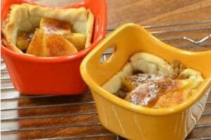 An orange and a yellow ramekin filled with baked apple tarts, cooling on a wire rack.