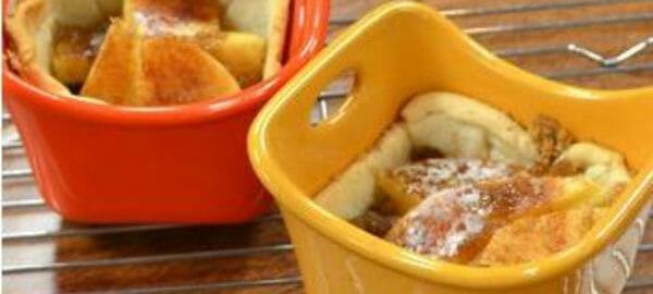 An orange and a yellow ramekin filled with baked apple tarts, cooling on a wire rack.