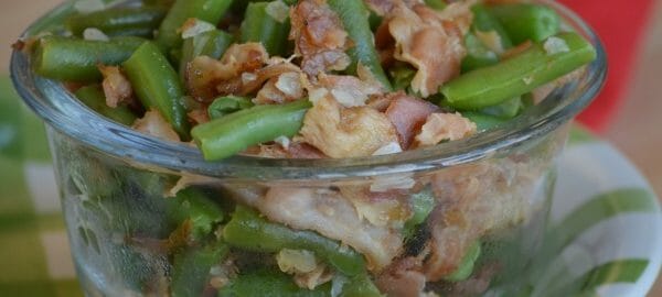 A clear glass ramekin filled with Bacon Green Beans, placed on a green and white plate.