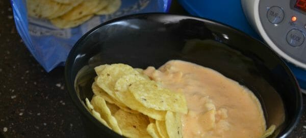 A black bowl with corn chips and Buffalo Chicken Dip, next to a blue bag of chips.