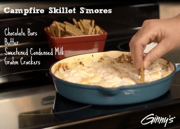 Campfire Skillet S'mores - Hand dipping a Graham cracker into a blue skillet filled with melted chocolate and marshmallows.
