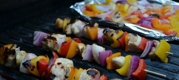 Three Chicken Shish Kabobs cooking on a grill, with more pieces on foil.