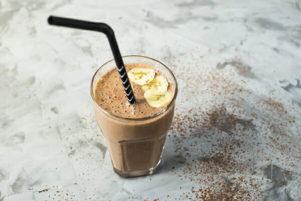 A clear soda fountain glass filled with a chocolate banana shake, topped with banana slices.