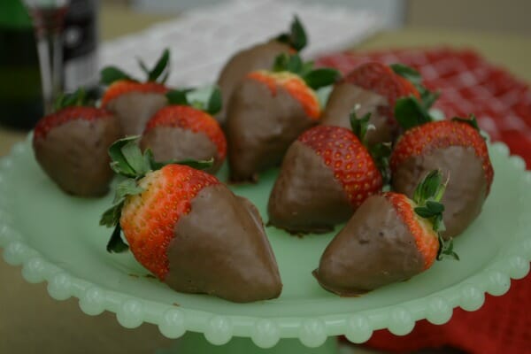 A white pedestal dish filled with whole chocolate covered strawberries with stems.
