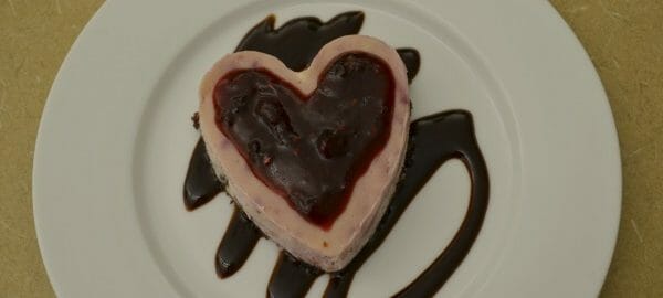 A white dessert plate with a Chocolate Raspberry Heart placed on swirls of chocolate syrup.