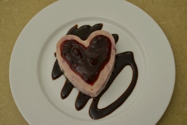 A white dessert plate with a Chocolate Raspberry Heart placed on swirls of chocolate syrup.