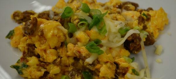 A white plate with a serving of Chorizo Scrambled egg casserole, topped with cheese and chopped green onions.