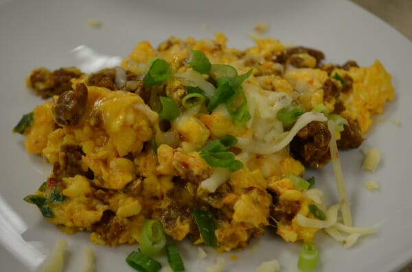A white plate with a serving of Chorizo Scrambled egg casserole, topped with cheese and chopped green onions.