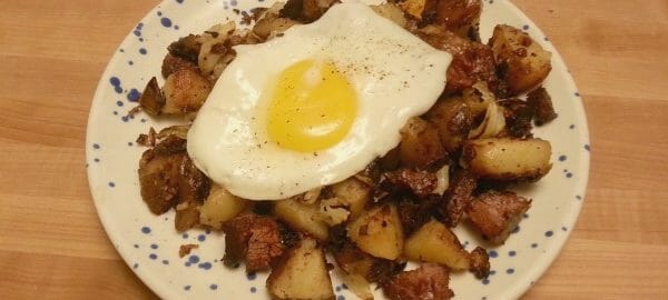 A blue speckled plate with a serving of Corned Beef Hash topped with a sunny-side-up egg.
