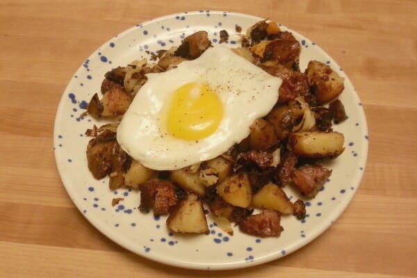 A blue speckled plate with a serving of Corned Beef Hash topped with a sunny-side-up egg.