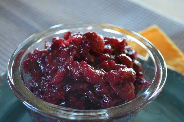 Close-up of a clear glass ramekin filled with Cranberry Sauce with Pineapple, placed on a blue plate.