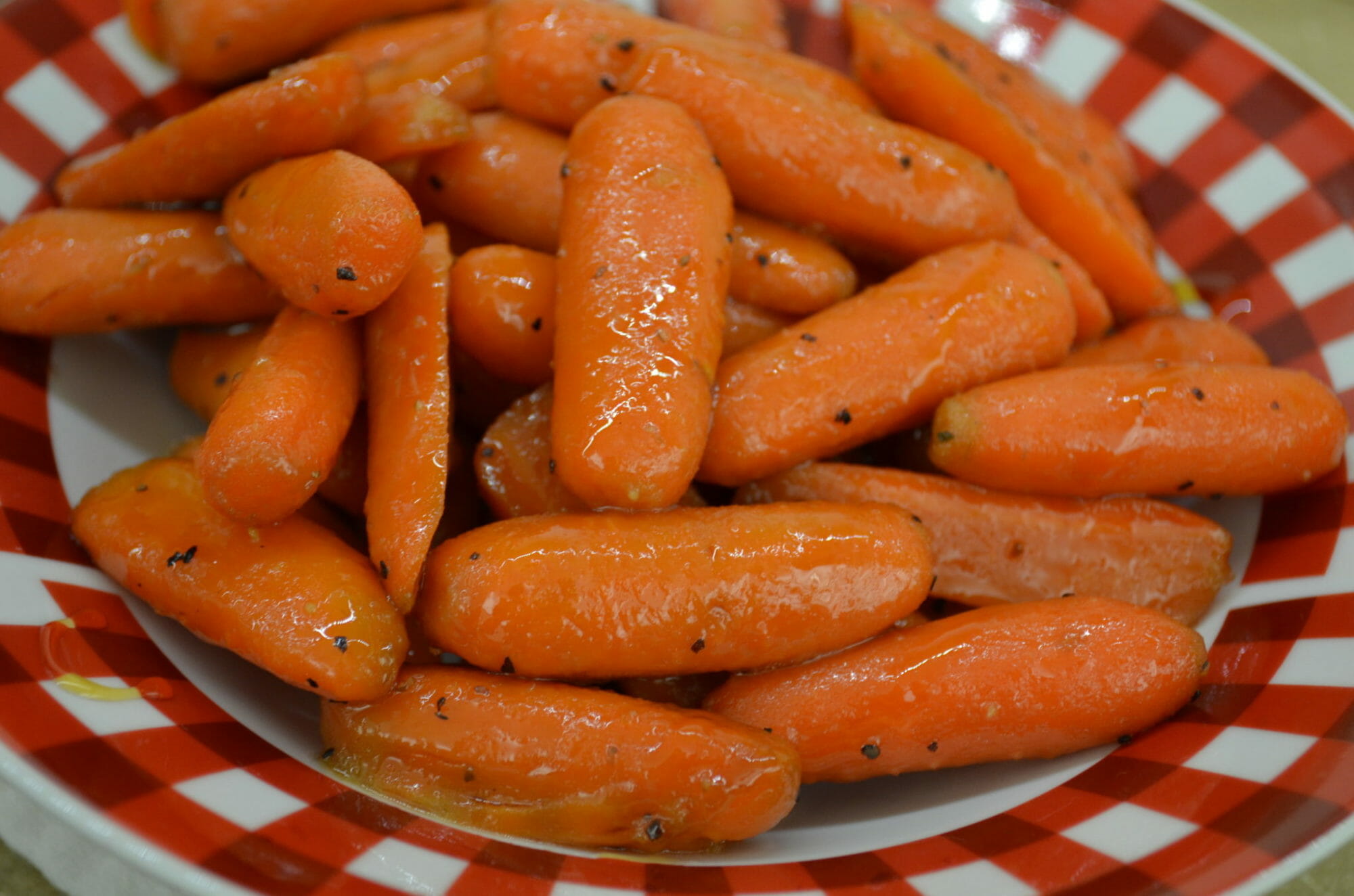 A red and white bowl filled with seasoned baby carrots.