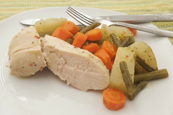 A white plate with a serving of Italian Chicken, carrots, potatoes, and green beans, with a knife and fork.