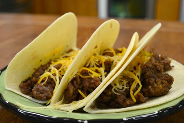 A green plate with three soft shell tacos topped with shredded cheese.