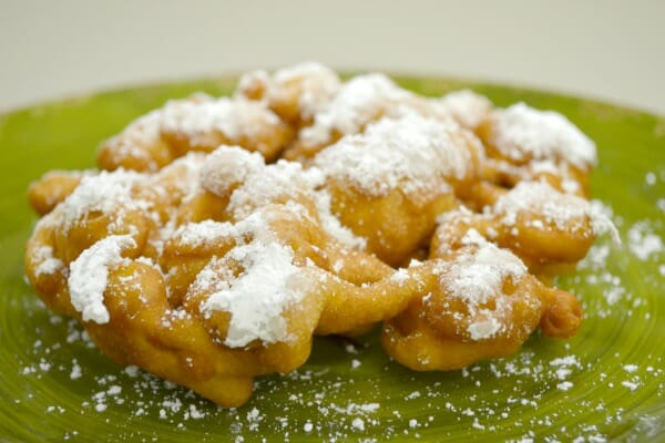 Close-up of a green plate with a Funnel Cake that is dusted with powdered sugar.