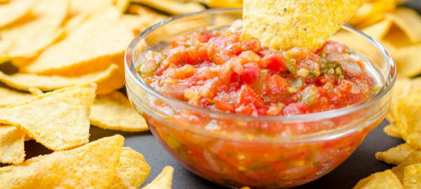 A clear glass bowl filled with colorful Garden Salsa, surrounded by crispy corn chips.