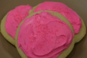 Three round sugar cookies topped with pink icing and red sugar crystals.