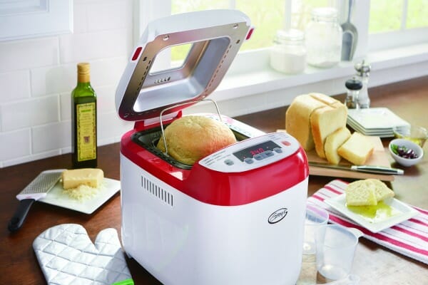 Ginny's red and white bread machine with a loaf of bread in the cooker, and one on a counter with cut slices.