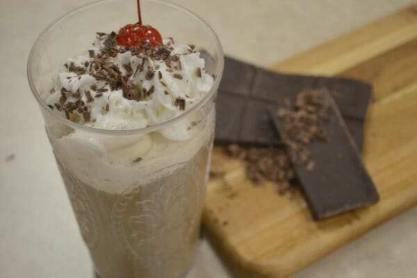 A clear glass filled with Italian Ice Cream Coffee, topped with whipped cream, shaved chocolate and a maraschino cherry.