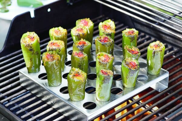 Several Jalapeno Poppers upright in a metal pan with holes, placed on a flaming grill.