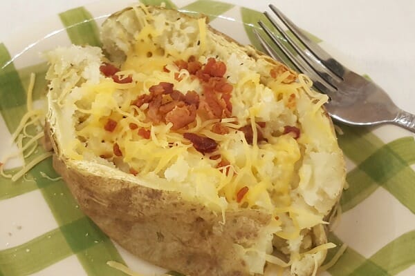 A microwave Baked Potato on a green and white plate, topped with bacon and shredded cheese.