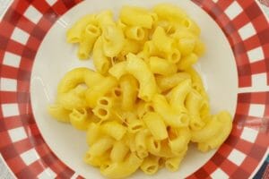 A red and white plate with a serving of golden Microwave Macaroni and Cheese.