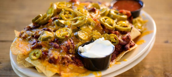 A white plate piled with Microwave Nachos, with two small bowls of sour cream and salsa.