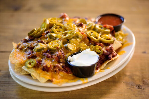 A white plate piled with Microwave Nachos, with two small bowls of sour cream and salsa.
