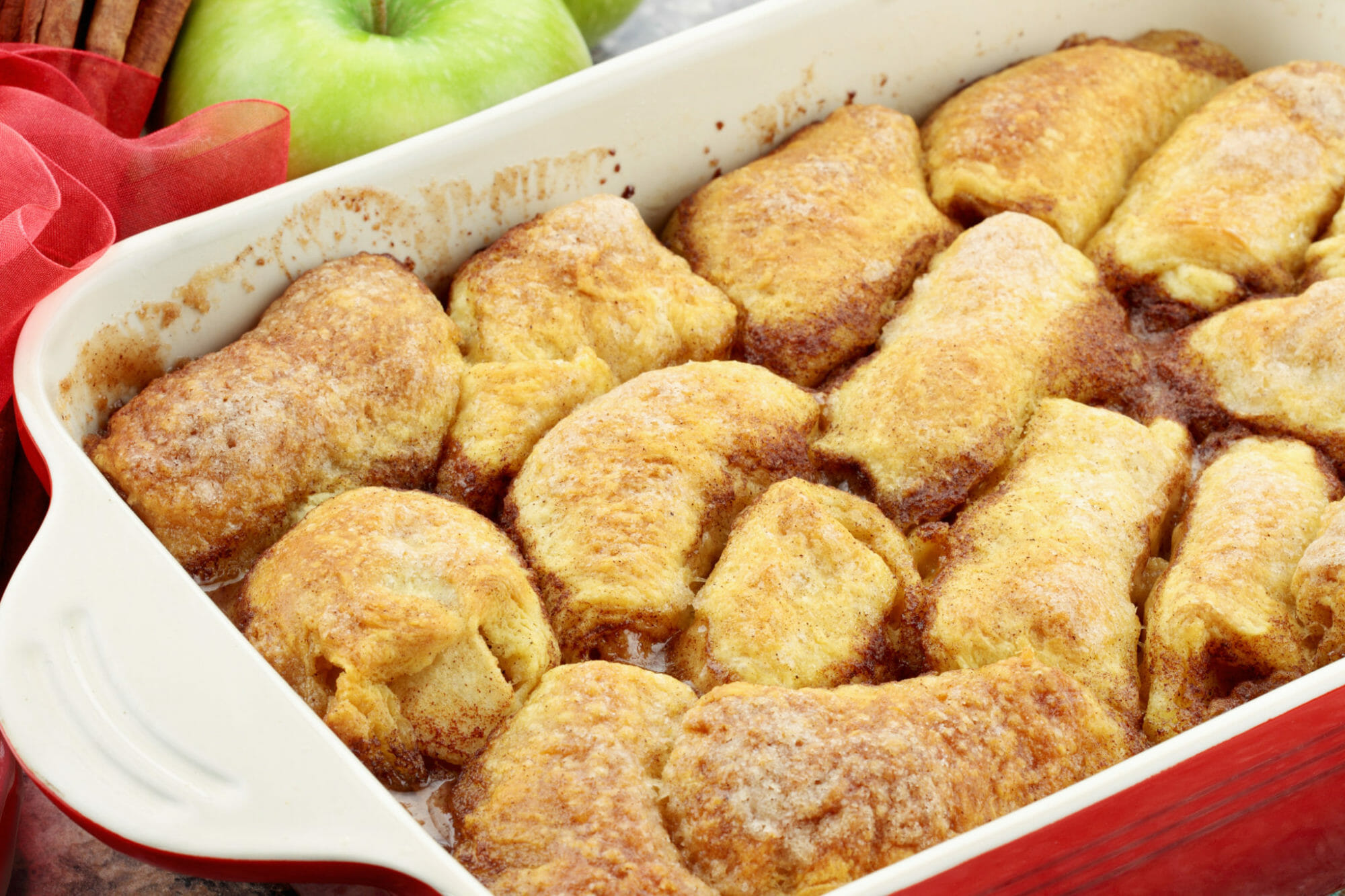 A white and red baking dish filled with Mountain Dew Apple Dumplings.