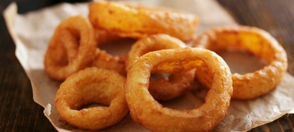 A pile of fried onion rings draining on brown parchment paper.