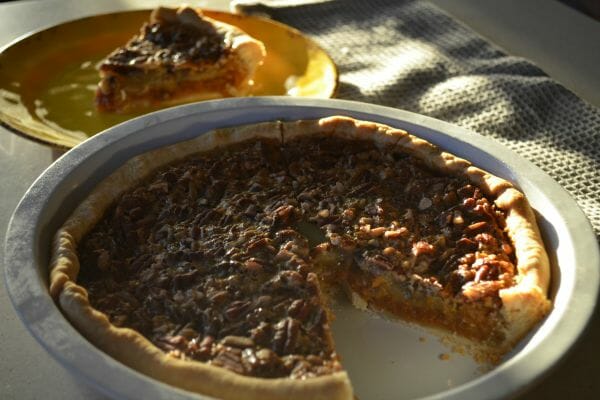 A Pecan Pumpkin Pie in a pie pan, with one slice placed on a yellow plate.