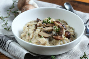 Close-up of a white bowl filled with Risotto topped with fresh mushrooms and thyme.