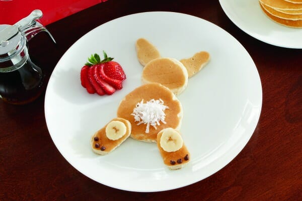 A white plate with small pancakes arranged in the shape of a bunny, with a side of sliced strawberries.