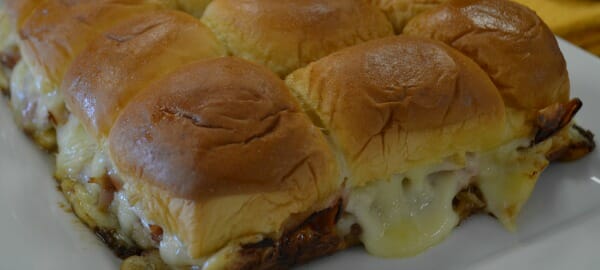 A white platter filled with baked ham and Swiss cheese sandwiches on Hawaiian rolls.