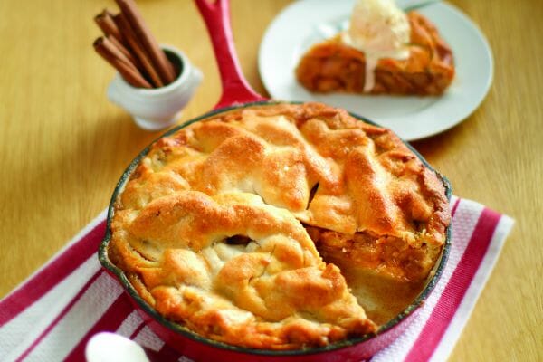 A red skillet filled with Skillet Apple Pie, with a sliced removed to a white plate, topped with a scoop of ice cream.