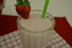 A Strawberry Cheesecake Milkshake in a fluted glass, with a green straw and a fresh strawberry garnish.