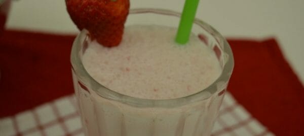 A Strawberry Cheesecake Milkshake in a fluted glass, with a green straw and a fresh strawberry garnish.