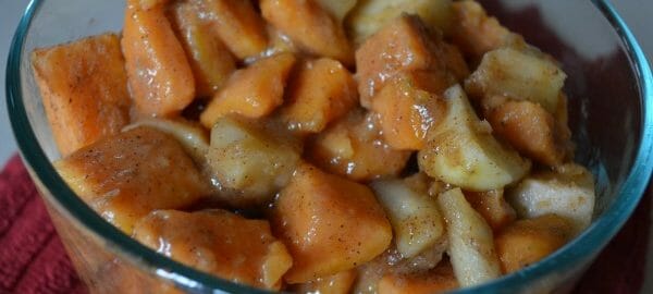 A clear glass bowl filled with glazed chunks of baked Sweet Potatoes and Apples.