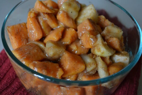 A clear glass bowl filled with glazed chunks of baked Sweet Potatoes and Apples.
