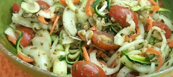 A green bowl filled with a salad of chunks and spirals of mixed raw vegetables, including zucchini and turnips.