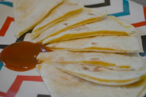 Eight quesadillas arranged on a colorful place with a red sauce in the center.