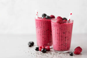 Two clear glasses filled with pink Berry Smoothies, topped with fresh raspberries and blueberries.