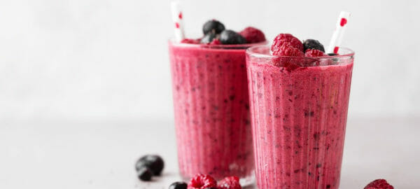 Two clear glasses filled with pink Berry Smoothies, topped with fresh raspberries and blueberries.