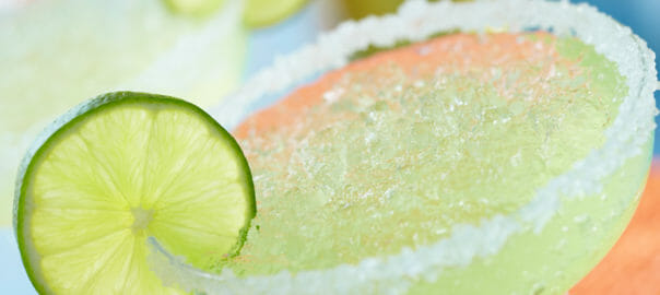 Close-up of a glass of chilled lime margarita rimmed with coarse sugar and a lime slice garnish.